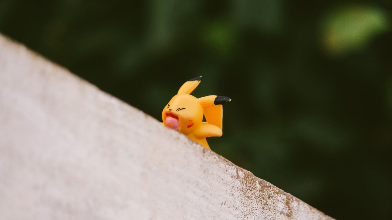 Vibrant yellow toy figurine playfully balancing on a ledge outdoors.