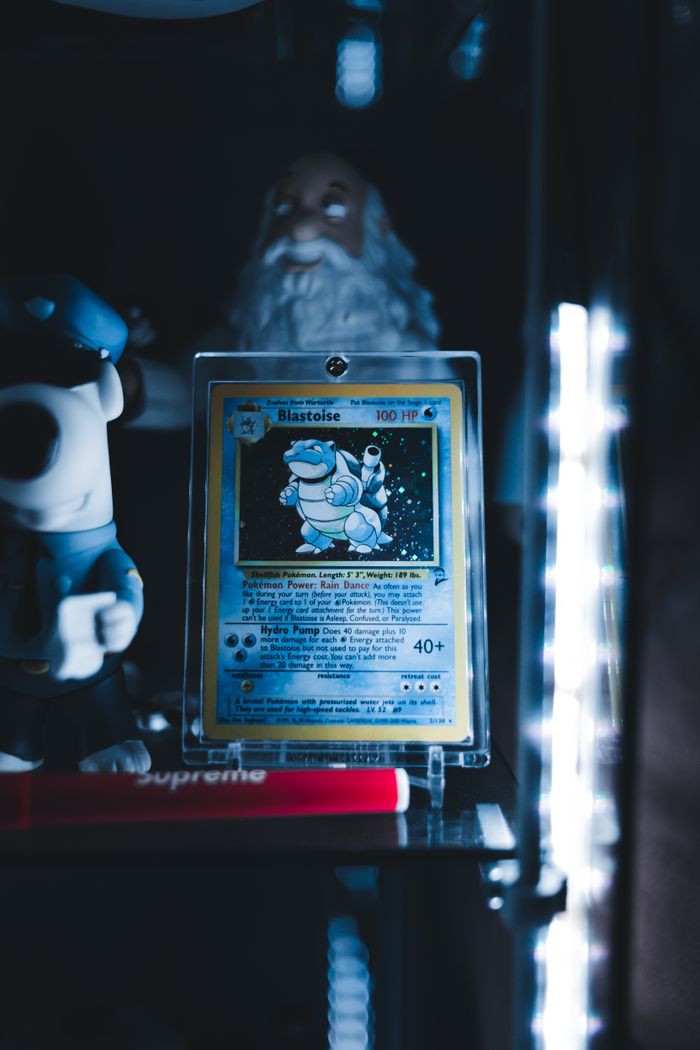 Blastoise Pokémon card in a protective case on display shelf with collectibles and ambient lighting.